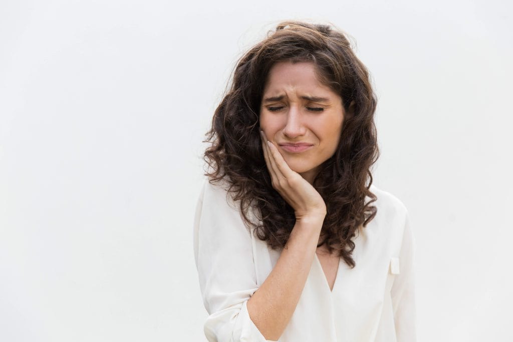 Mujer joven con sensibilidad dental llevándose la mano a la mejilla por un pinchazo de dolor