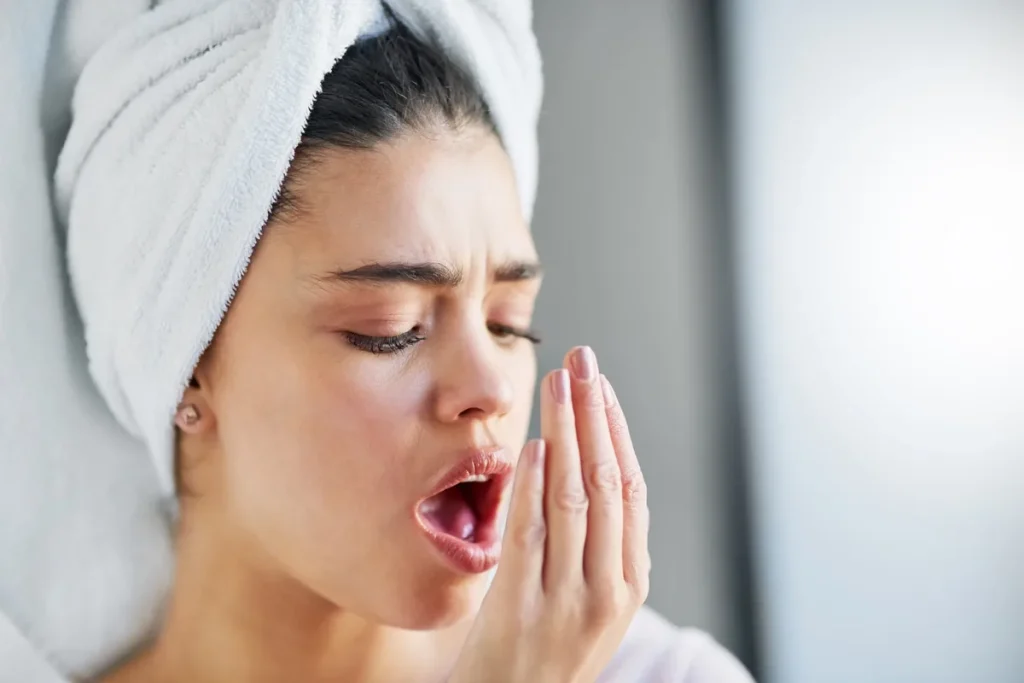 Mujer comprobando su aliento con la mano: el mal aliento o halitosis suele tener origen en la boca